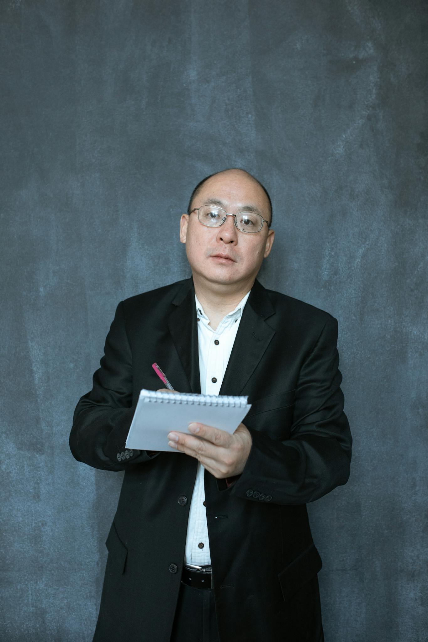 A focused businessman in formal attire holding a notebook against a neutral background.